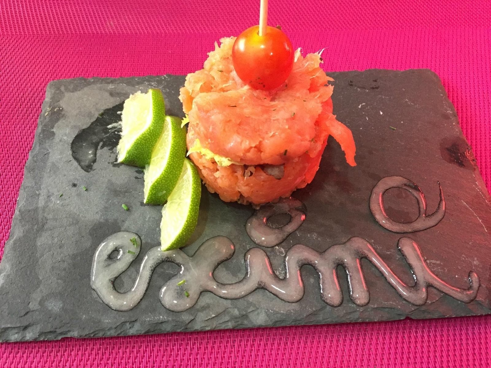 Tàrtar de salmó sobre pissarra amb el nom Eximi escrit amb salsa